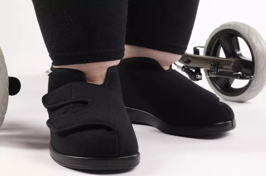 Varomed Genua Verbandschuh in Schwarz, Weite L, getragen an einem Fuß. Ideal für empfindliche, geschwollene oder bandagierte Füße. Bequem und atmungsaktiv, mit verstellbarem Klettverschluss für eine optimale Passform. Hersteller: Varomed, Art. 60920